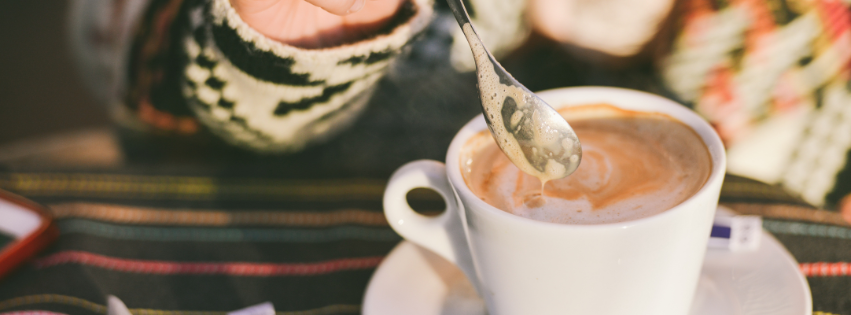 A spoon rests above a cup of coffee with cream swirling, symbolizing smart systems and effortless productivity.